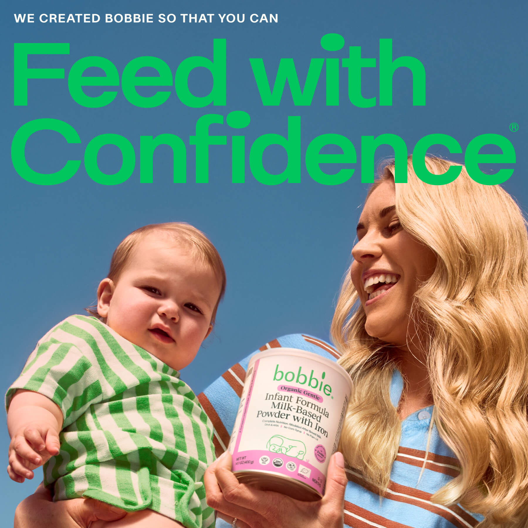 Woman holding a baby and a Bobbie Organic Gentle Infant Milk-Based Powder with Iron formula container with a blue sky background. Feed with confidence.