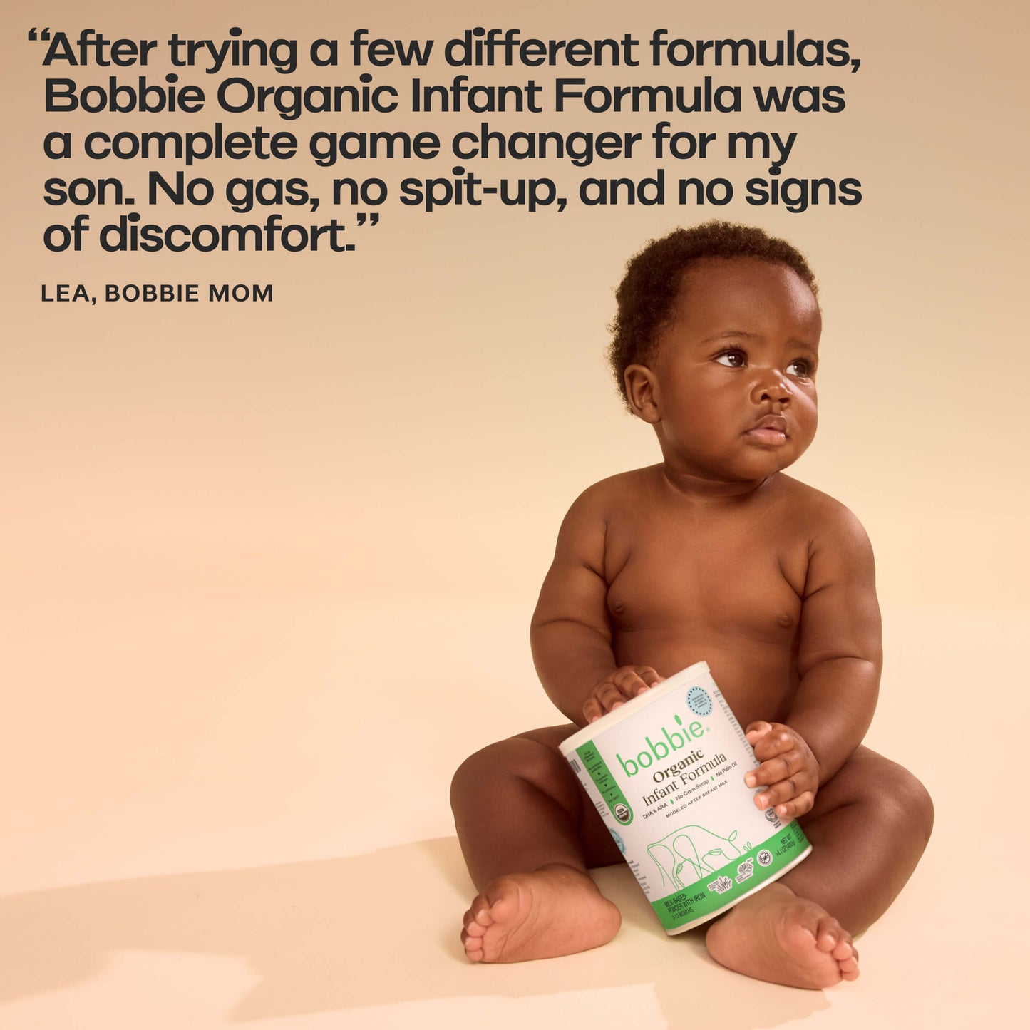 Baby holding a Bobbie Organic Infant Formula container with a testimonial quote on a beige background.
